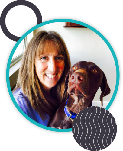 A woman with long brown hair, smiling and posing indoors with a brown dog that has a blue collar. The image, perhaps taken by her veterinarian, features a teal circular border adorned with abstract geometric shapes in the corners.