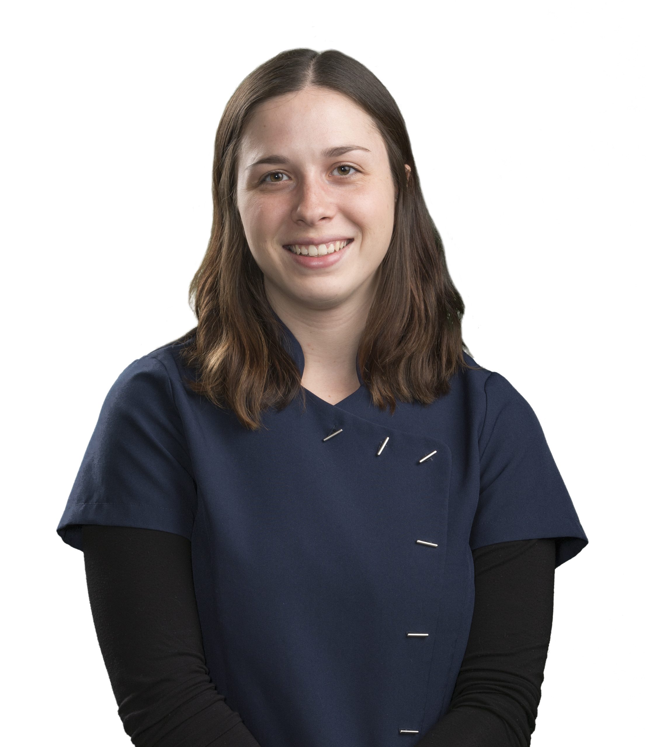 A person with shoulder-length brown hair, wearing a dark navy blue outfit over a black long-sleeve shirt, is smiling warmly while looking at the camera. The background is plain white, giving them a professional demeanor that evokes the trusted presence of a dedicated veterinarian.