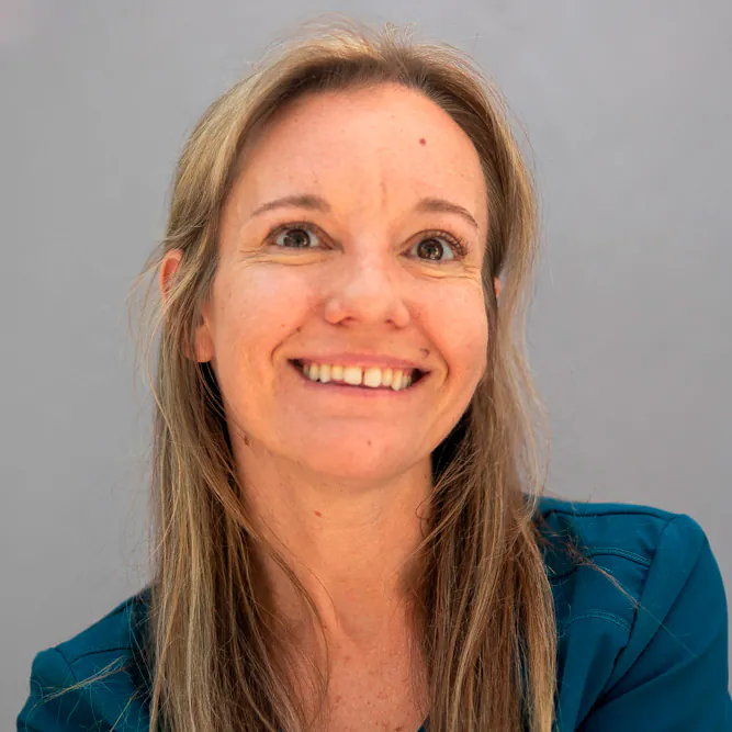 A woman with long light brown hair and a teal top smiles warmly while looking slightly upward, against a plain light gray background.
