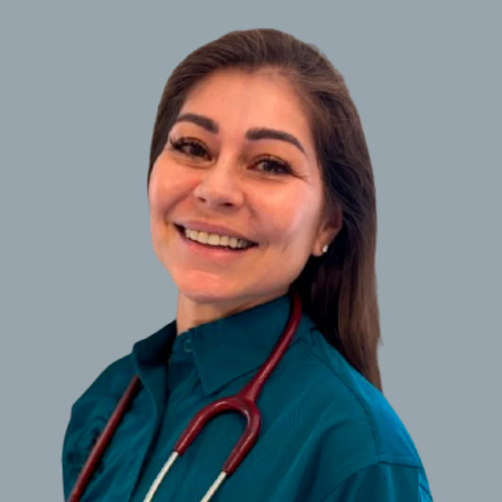 A woman with long brown hair, wearing a teal shirt and a red stethoscope around her neck, smiles at the camera against a plain grey background.